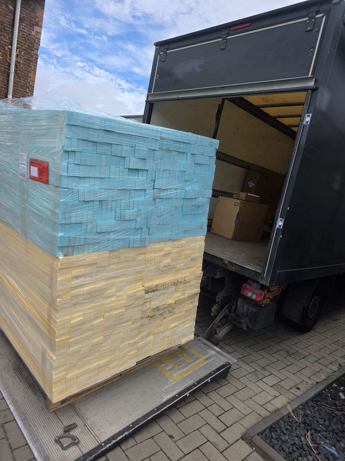 Blaue und gelbe Dämmstoffblöcke auf einer Palette an der Laderampe eines Transportfahrzeugs