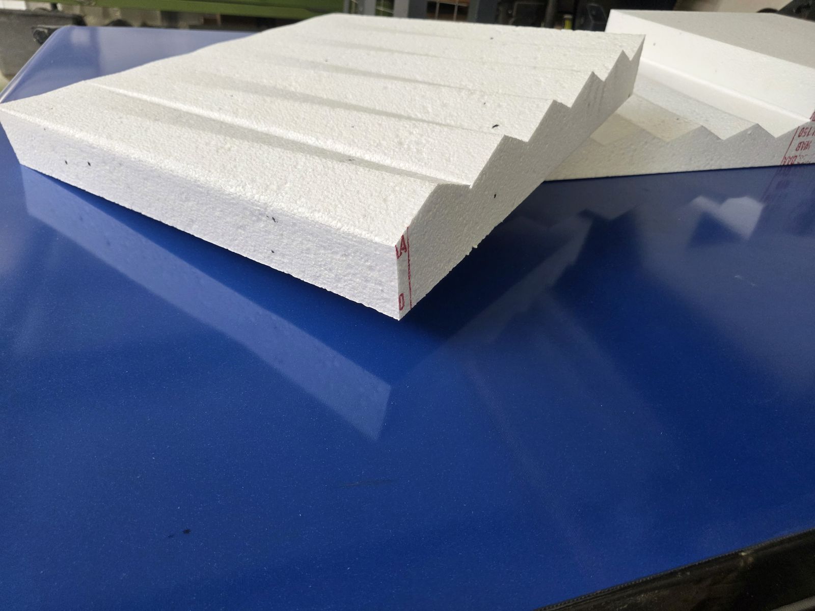 Weiße EPS-Dämmplatten mit CNC-gefrästem Stufenprofil auf blauer Arbeitsfläche